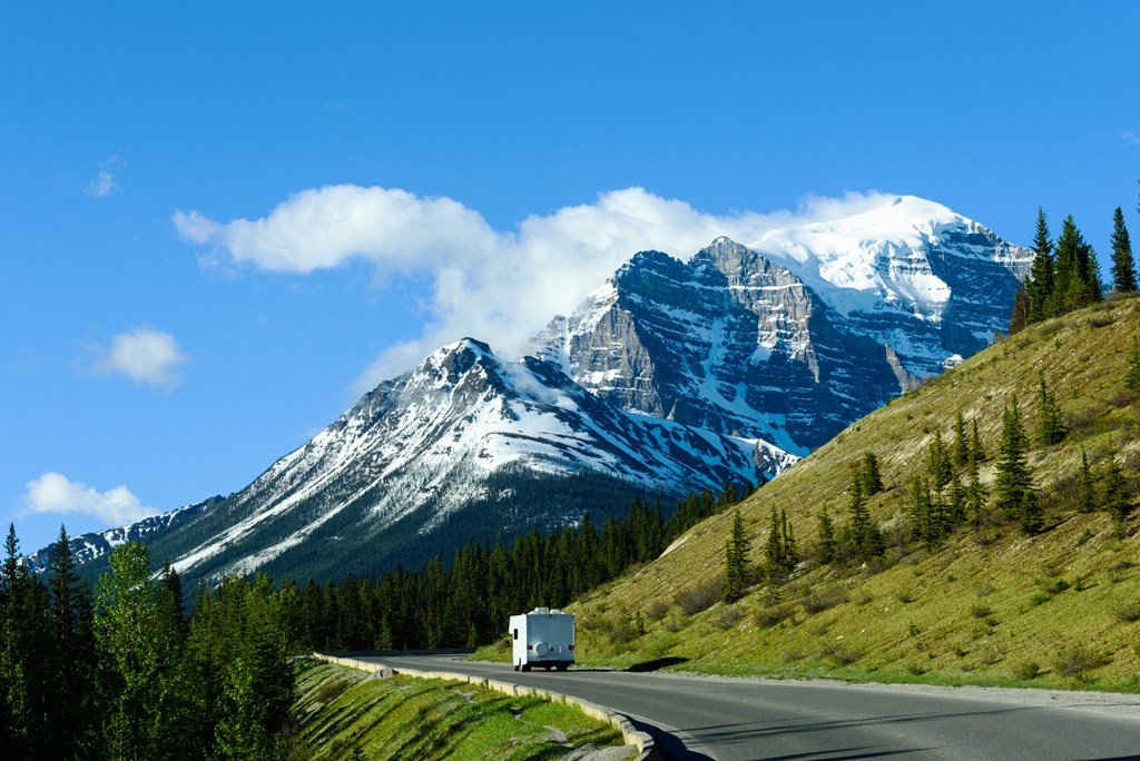 An RV on the road in Banff Canada with mountains in the distance.