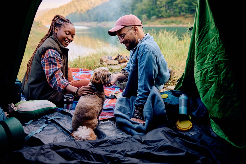 A young couple enjoys tenting camping at a KOA campground with their small dog.