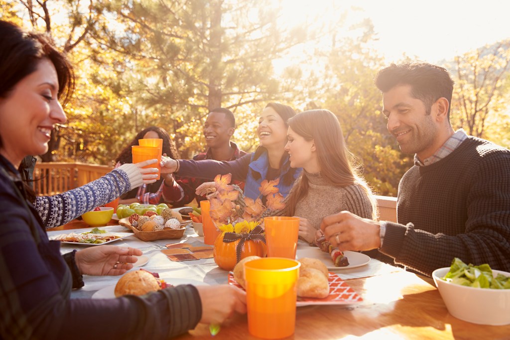 Group of happy friends eat and drink at a table at a barbecue in fall.