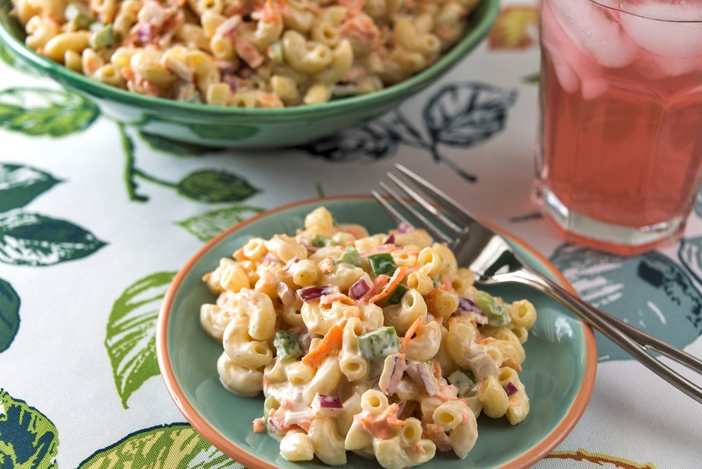 A serving of traditional elbow macaroni salad is served with a refreshing glass of cold pink lemonade.