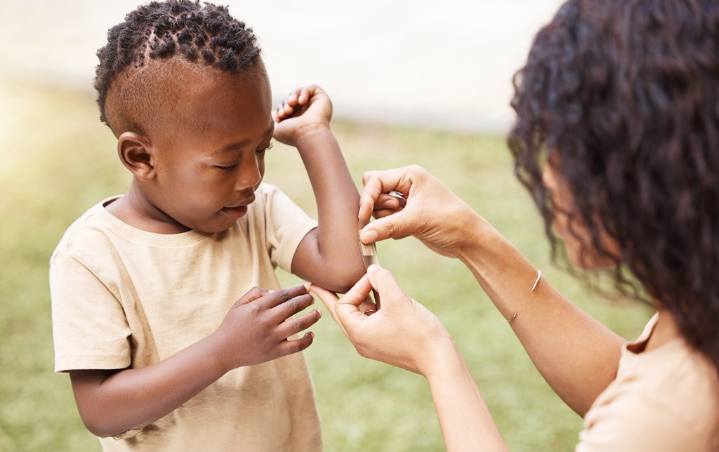 Mother putting a bandaid on a young boy's elbow.