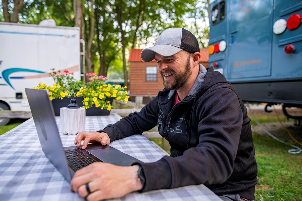 A man working on a laptop at a picnic table outside of his RV.
