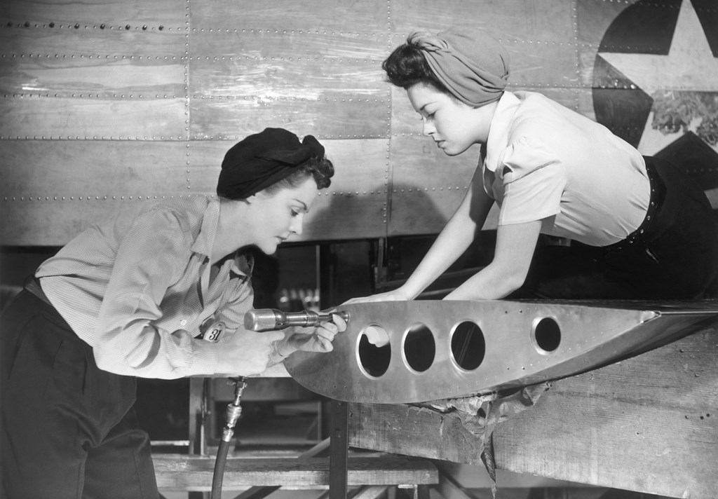 A vintage black and white photo of two women working on a military aircraft.