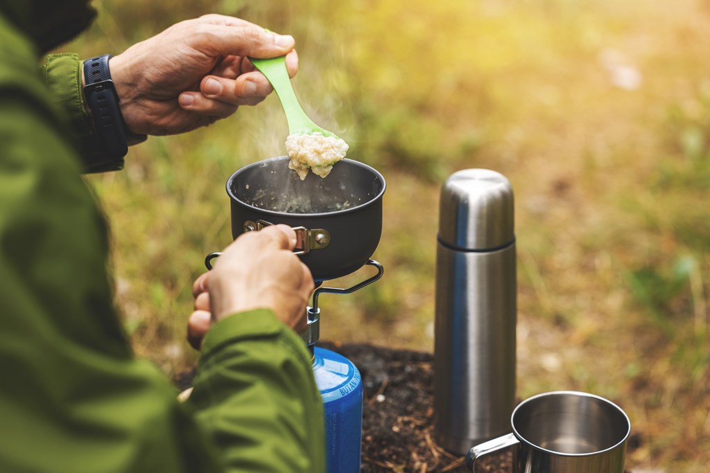 Hiker preparing oatmeal porridge outdoors on gas burner.