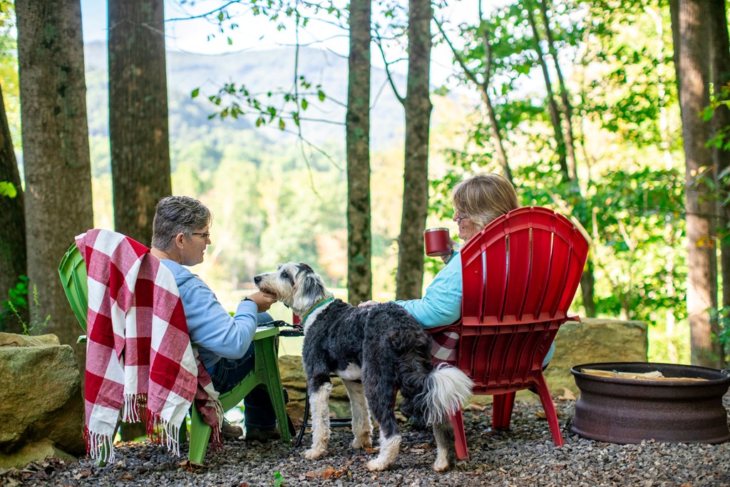 Two woman sit in Adirondack chairs with their dog between them at a KOA campground. 