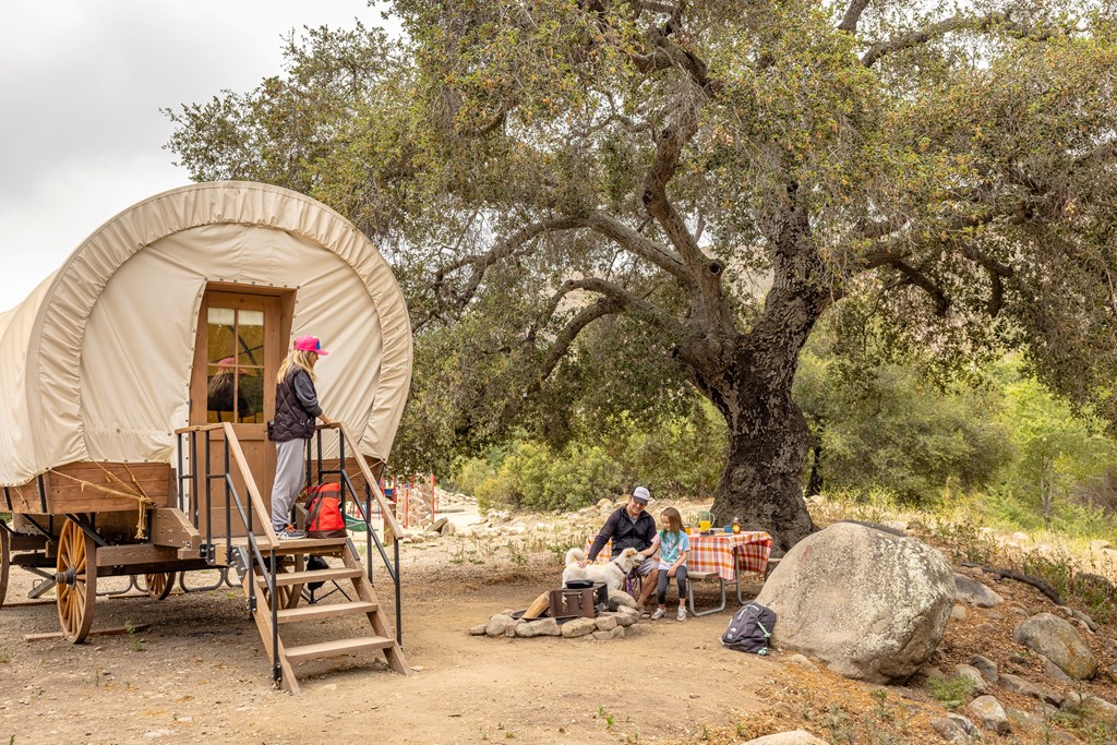 A family of three with a young child enjoys a unique accommodation at a KOA campground. This fully-furnished Conestoga wagon is a fun way to stay at a campground.